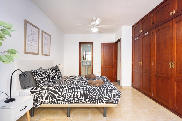 A bedroom with a bed, a desk, a wardrobe, and a ceiling fan.