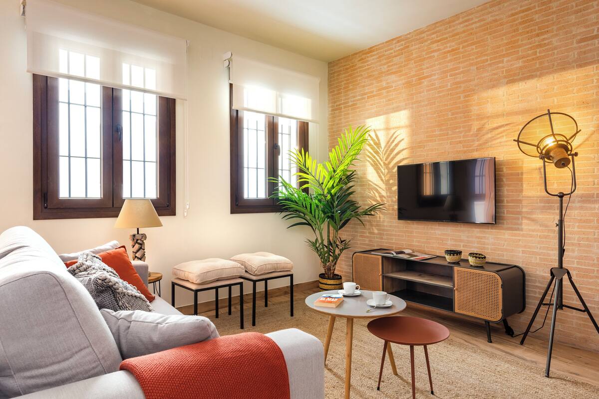 A modern living room with a sofa, a coffee table, a TV mounted on a brick wall, and a potted plant.