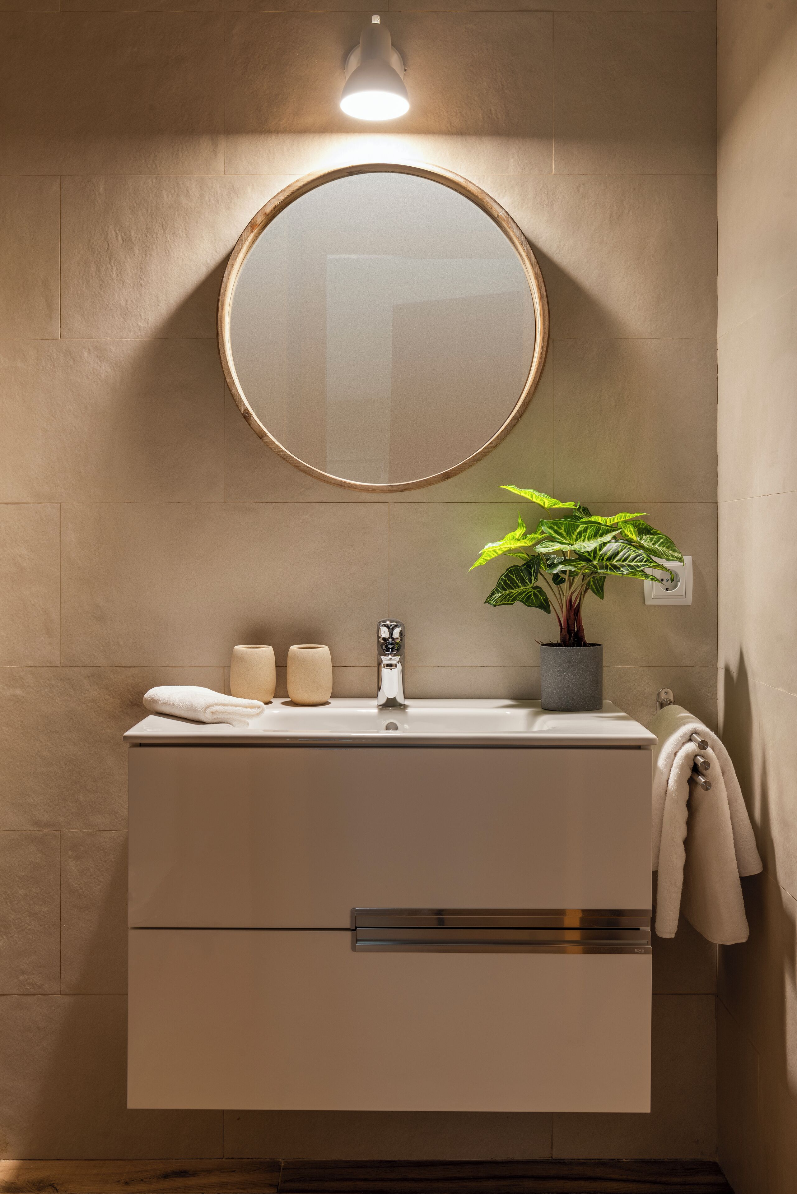 Un bagno con uno specchio rotondo, un lavandino, una pianta in vaso e un porta asciugamani.