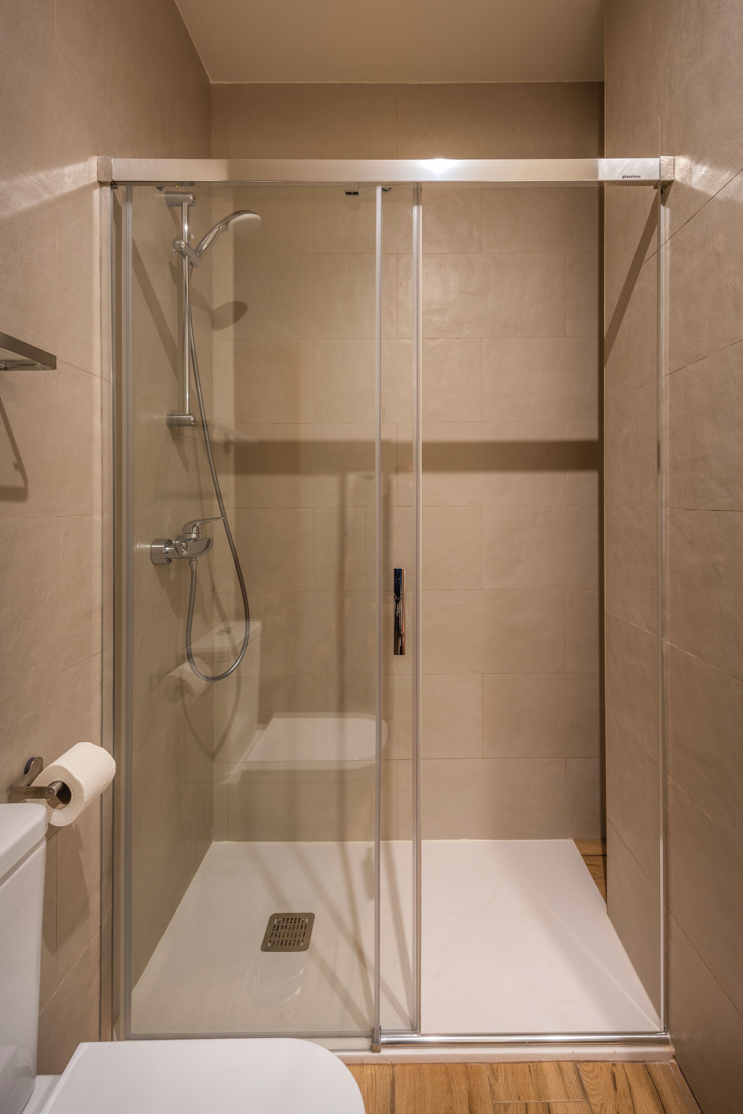 Eine Duschkabine mit Glaswänden, eine Toilette und ein Papierhandtuchhalter.