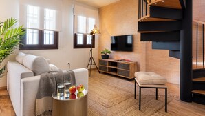 A modern living room with a sofa, a coffee table with apples, a TV mounted on a brick wall, and a staircase with wooden steps. - MH Apartments Central Sevilla (Seville)