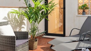 A patio with a wicker chair, a lounge chair, a table with a magazine, and a potted plant. - MH Apartments Central Sevilla (Seville)