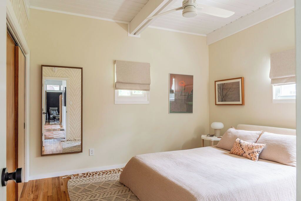 Une chambre avec un grand lit, un ventilateur de plafond, un miroir et une fenêtre avec un store.