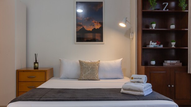 A neatly made bed with a dark throw, a nightstand with a bottle and a small plant, and a wall-mounted shelf with decorative items. - 3 minutes from Ipanema beach | JN202 (Rio de Janeiro)