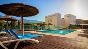 A pool area with lounge chairs and umbrellas, a building with 'Hotel Femenina & Congressos' signage, and a clear sky.