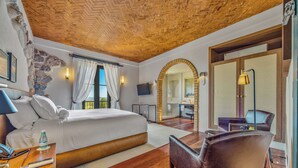 A hotel room with a wooden ceiling, a large bed, a sitting area with a chair, and a bathroom visible through an archway. - Hotel Borgo Del Vino (Areal)