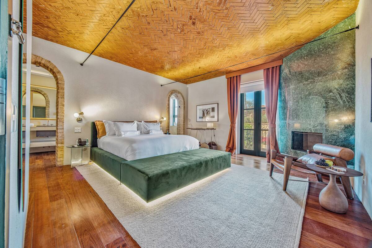 A modern bedroom with a large bed, a green bench, a wooden coffee table, and a stone wall.