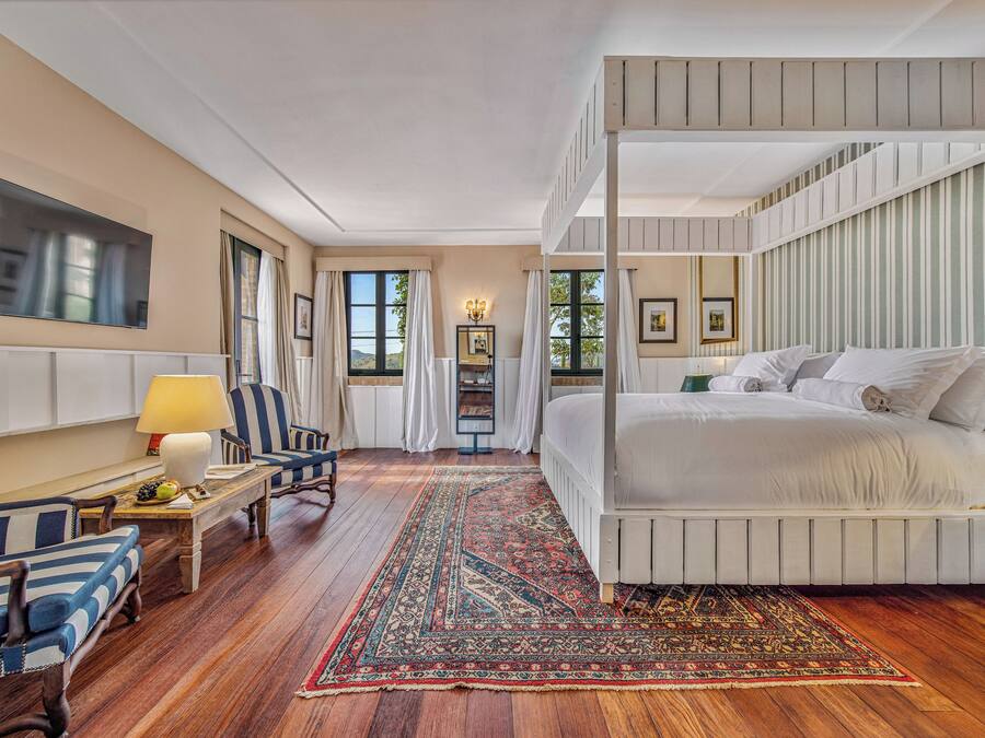 Un dormitorio con cama con dosel, suelo de madera, alfombra grande, televisor y escritorio con lámpara.