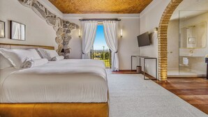 A bedroom with a large bed, stone wall, wooden ceiling, and a view through curtains. - Hotel Borgo Del Vino (Areal)