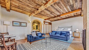 A spacious living area with a wooden ceiling, a blue sofa set, a dining table with chairs, and a patterned rug. - Hotel Borgo Del Vino (Areal)