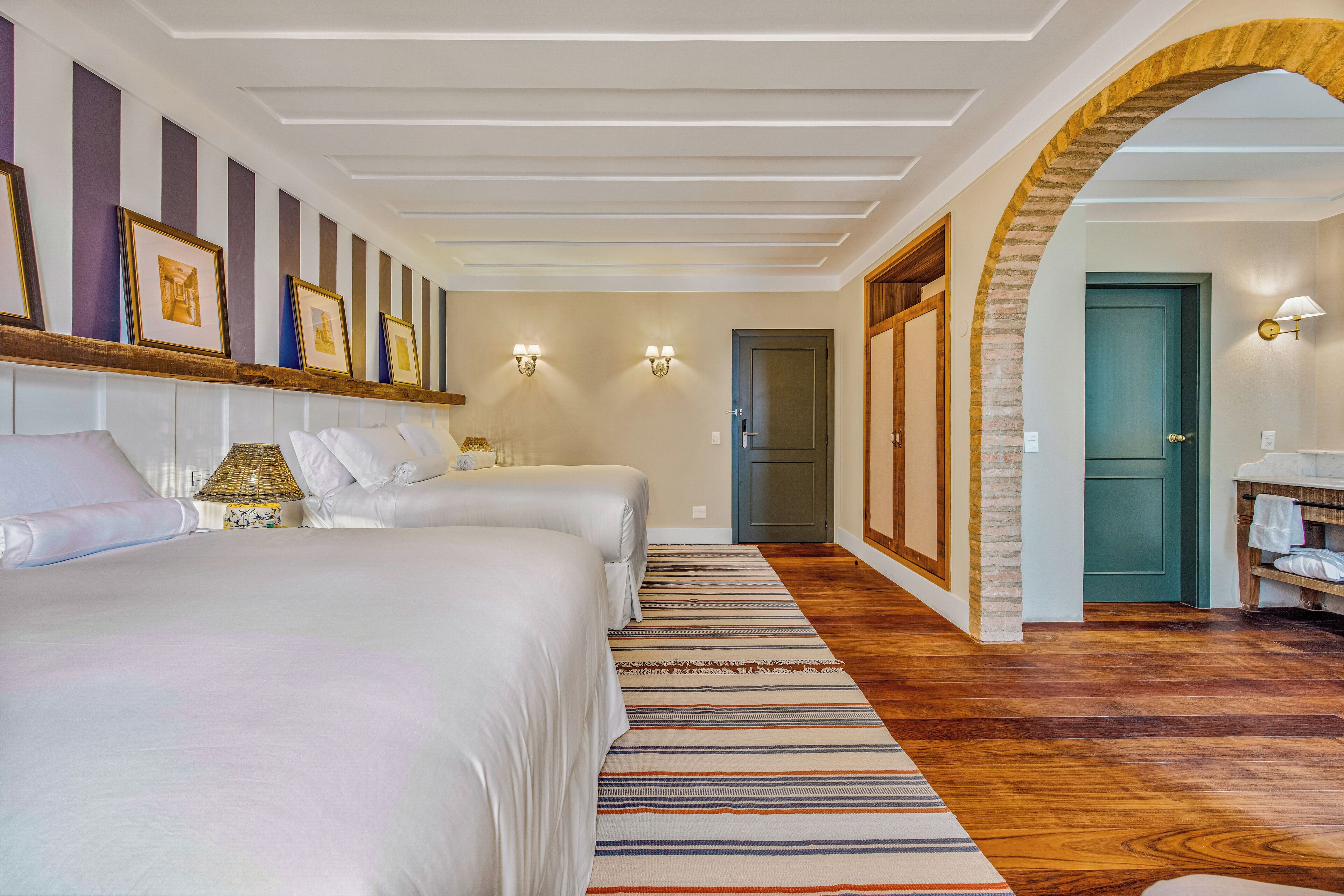 A hotel room with two beds, a striped rug, and a hallway leading to a door.