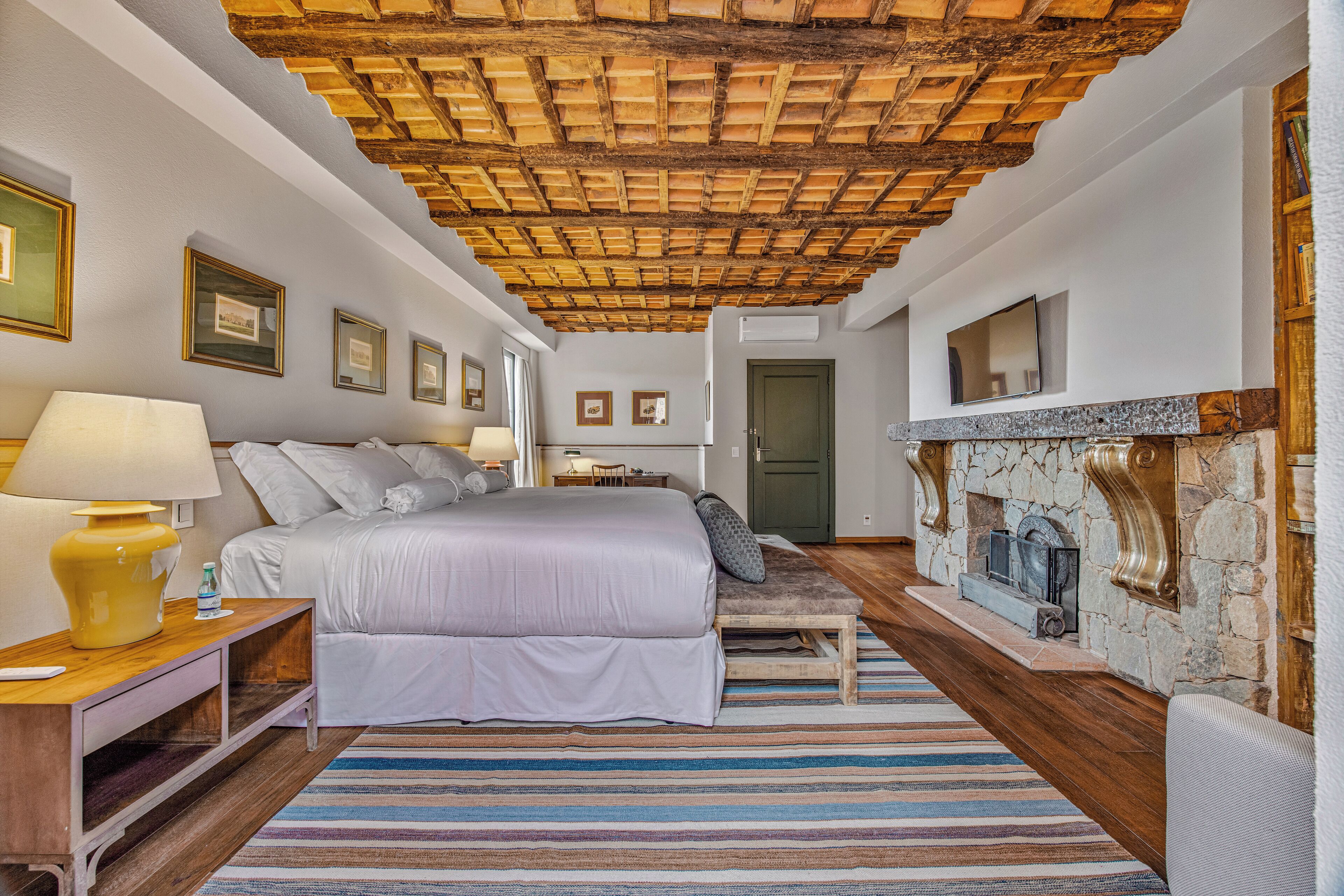 A bedroom with a bed, bedside table, lamp, and a stone fireplace.