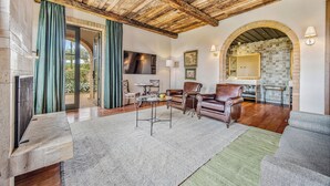 A spacious living room with a wooden ceiling, a stone fireplace, and a large TV mounted on the wall. - Hotel Borgo Del Vino (Areal)