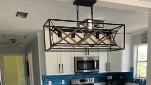 A modern kitchen with white cabinets, a stainless steel microwave, and a large island with bar stools. - Cabana Escape – Waterfront Oasis with Heated Pool and Spacious Outdoor Living (St. Augustine)