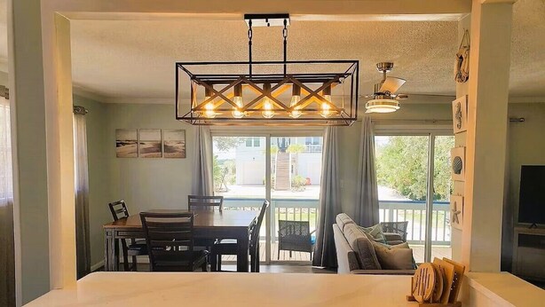 A modern kitchen with a large island, a dining area with a table and chairs, and a balcony with a view. - Cabana Escape – Waterfront Oasis with Heated Pool and Spacious Outdoor Living (St. Augustine)