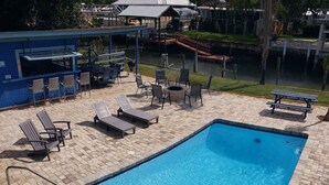 A rectangular swimming pool with a tiled deck, surrounded by lounge chairs and a barbecue area. - Cabana Escape – Waterfront Oasis with Heated Pool and Spacious Outdoor Living (St. Augustine)