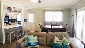 A living room with a sofa, two chairs, a dining table, and a kitchen area with a bar stool. - Cabana Escape – Waterfront Oasis with Heated Pool and Spacious Outdoor Living (St. Augustine)