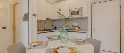 A compact kitchen with white cabinets, a microwave, and a dining table set for two with plates and glasses.