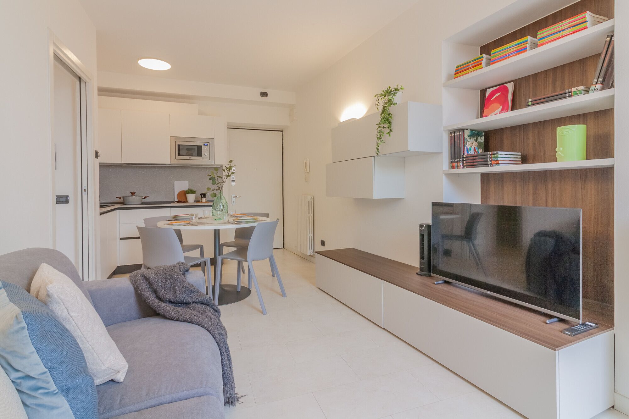 Un espace de vie compact comprenant un canapé, une table à manger avec des chaises, un téléviseur et une bibliothèque.