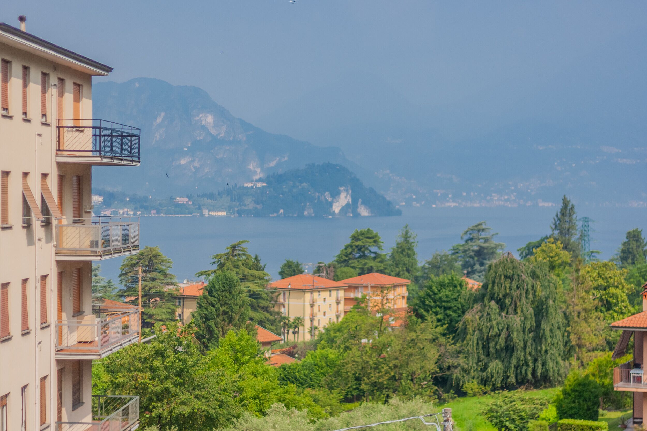 A residential area with multi-story buildings, balconies, and a view of a lake with mountains in the background.