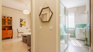 Una habitación de hotel moderna con ducha de vidrio, un armario de madera, una mesa de comedor con sillas y un espejo grande en la pared.