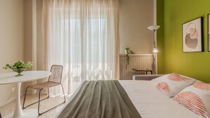 Una habitación de hotel con cama, escritorio, silla, lámpara y ventana con cortinas.