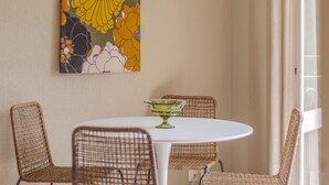 Un comedor con sillas de mimbre, una mesa blanca y una obra de arte floral en la pared.