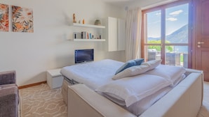 Ein Hotelzimmer mit Bett, Fernseher, Bücherregal und Blick ins Freie.