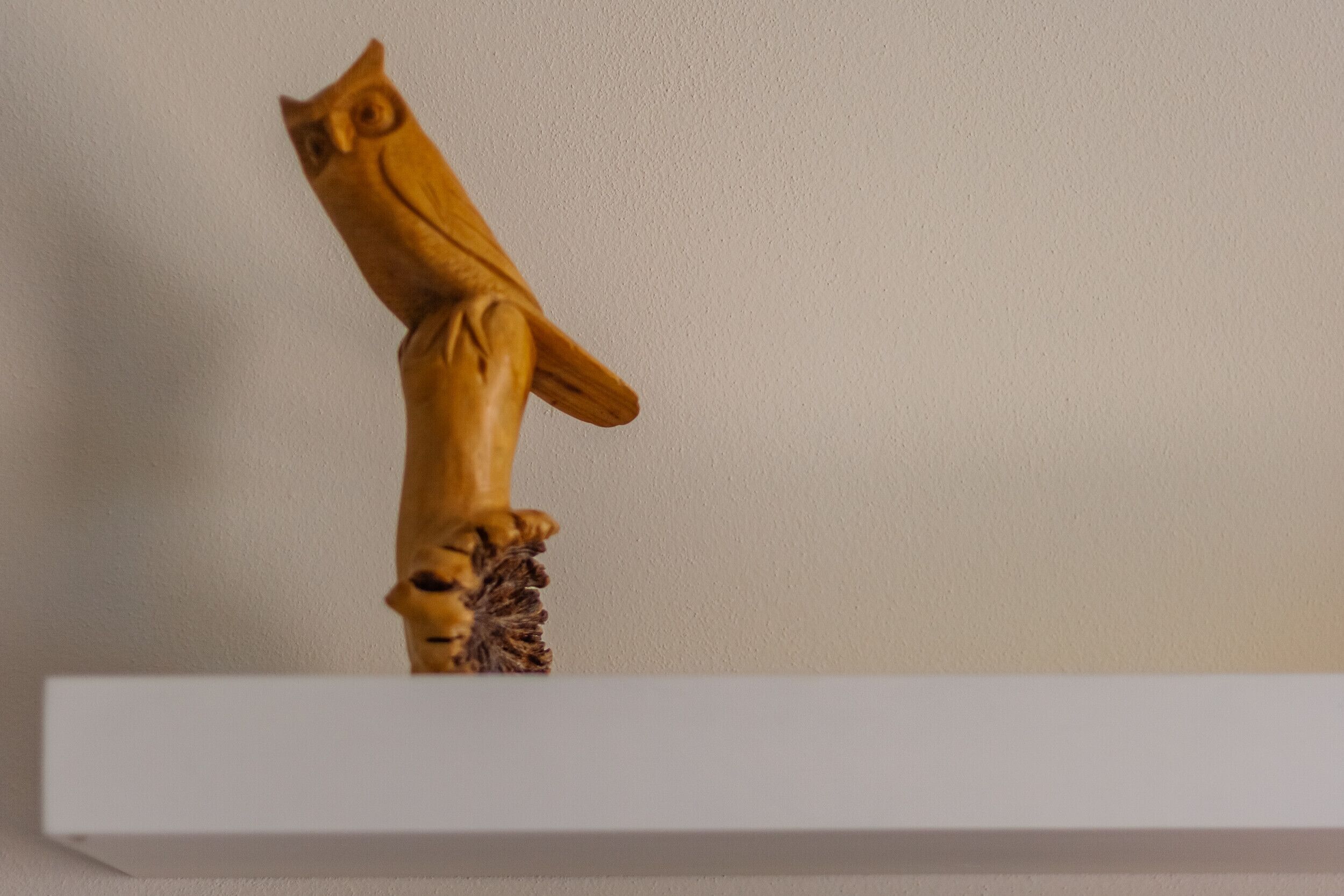 Una escultura de madera de un búho sobre un estante blanco frente a una pared lisa.