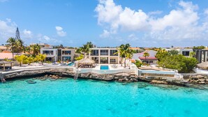 A resort with a pool area, palm trees, and buildings with balconies overlooking the water. - Kas di Bon Beis - Spacious Oceanfront Villa with Full A/C (Kralendijk)