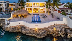 A modern resort with a pool, lounge chairs, and a thatched-roof outdoor seating area. - Kas di Bon Beis - Spacious Oceanfront Villa with Full A/C (Kralendijk)