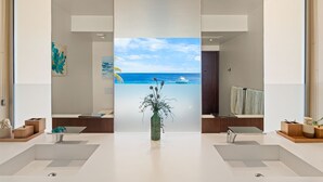 A modern bathroom with a large window, a central sink, and a decorative plant. - Kas di Bon Beis - Spacious Oceanfront Villa with Full A/C (Kralendijk)