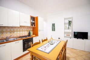 Cozinha moderna com armários brancos, bancada de madeira e mesa de jantar posta com um jogo americano e uma garrafa.