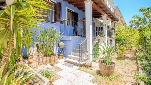 A two-story house with a blue exterior, a wooden staircase, and a garden with various plants. - Sa Sterlizia by All4sardinia  (Cardedu)
