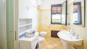 A compact bathroom with a washing machine, toilet, and sink. - Sa Sterlizia by All4sardinia  (Cardedu)