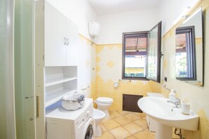 A compact bathroom with a washing machine, toilet, and sink. - Sa Sterlizia by All4sardinia  (Cardedu)