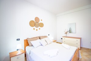 Quarto bem organizado com cama, mesas de cabeceira, penteadeira e um enfeite na parede.