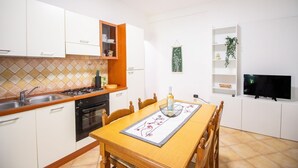 A modern kitchen with white cabinets, a wooden countertop, and a dining table set with a placemat and a bottle.