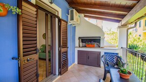 A balcony with a grill, a chair, and a table with a potted plant. - Sa Sterlizia by All4sardinia  (Cardedu)