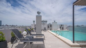 Un espace piscine sur le toit, avec des chaises longues, une piscine et une vue sur la ville.
