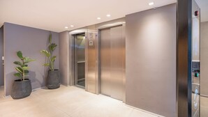 Un espace ascenseur moderne, agrémenté de deux plantes en pot, d’une porte d’ascenseur métallique et d’un panneau de commande.