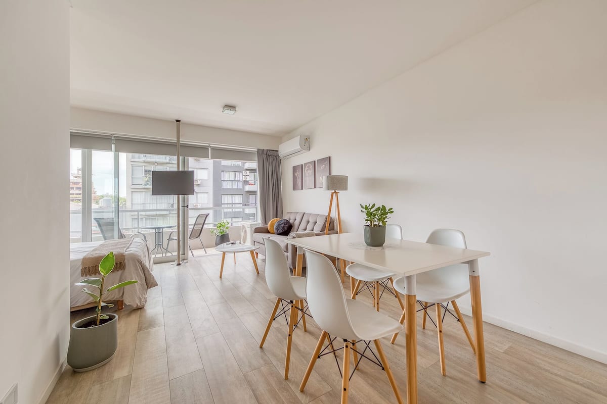 Een moderne woonkamer met een eettafel, stoelen, een bank en een groot raam.