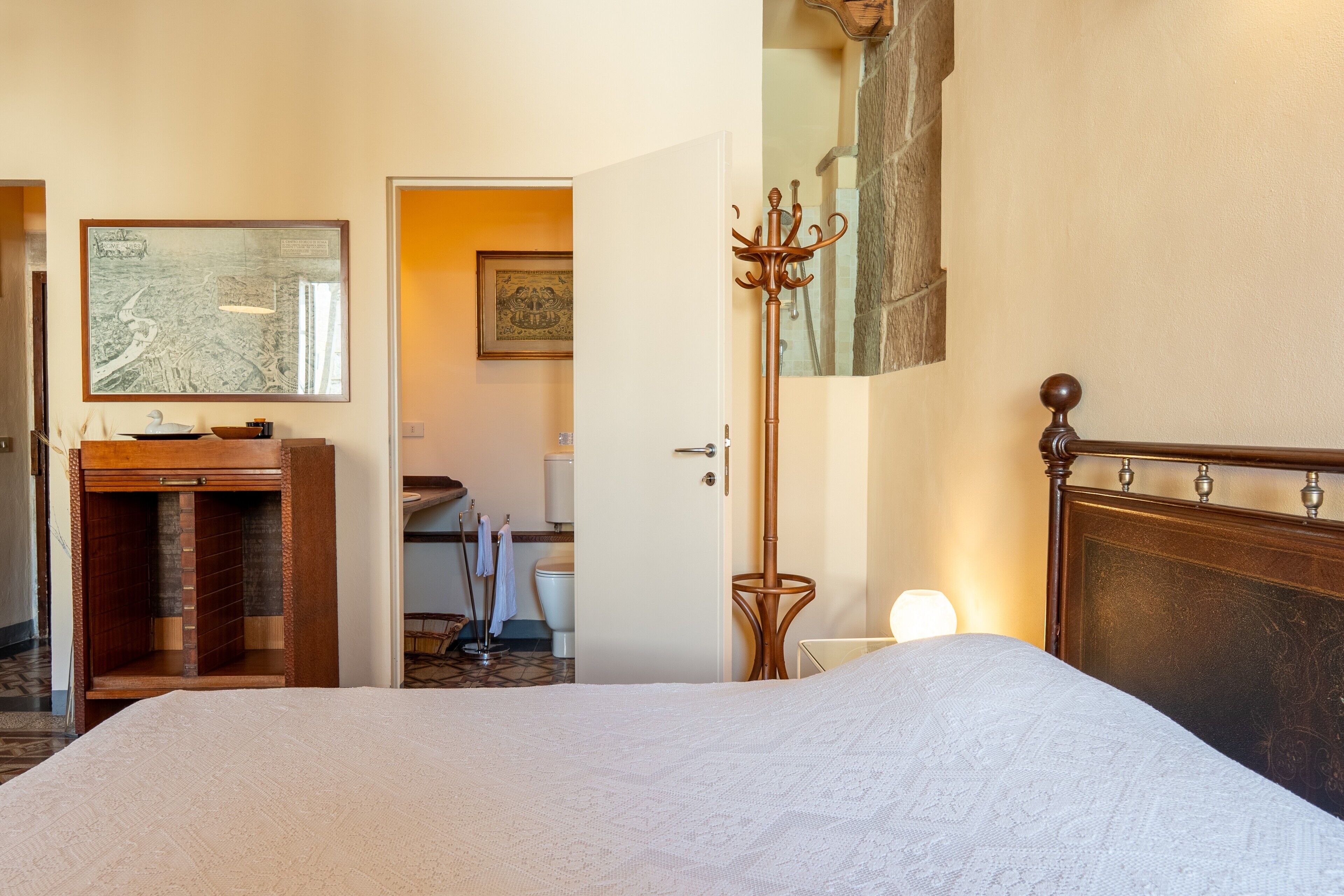 Ein Hotelzimmer mit einem Bett, einem Holzschrank, einem Kleiderständer, einem Spiegel und einem durch eine offene Tür einsehbaren Badezimmer.