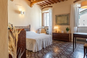 A bedroom with a bed, a chair, a dresser, a lamp, and a window with curtains.