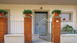 A gated entrance with a blue door, a brick wall, and a small window with a potted plant. - Charming tourist apartment near historic center of Montepulciano. Holiday home. (Montepulciano)