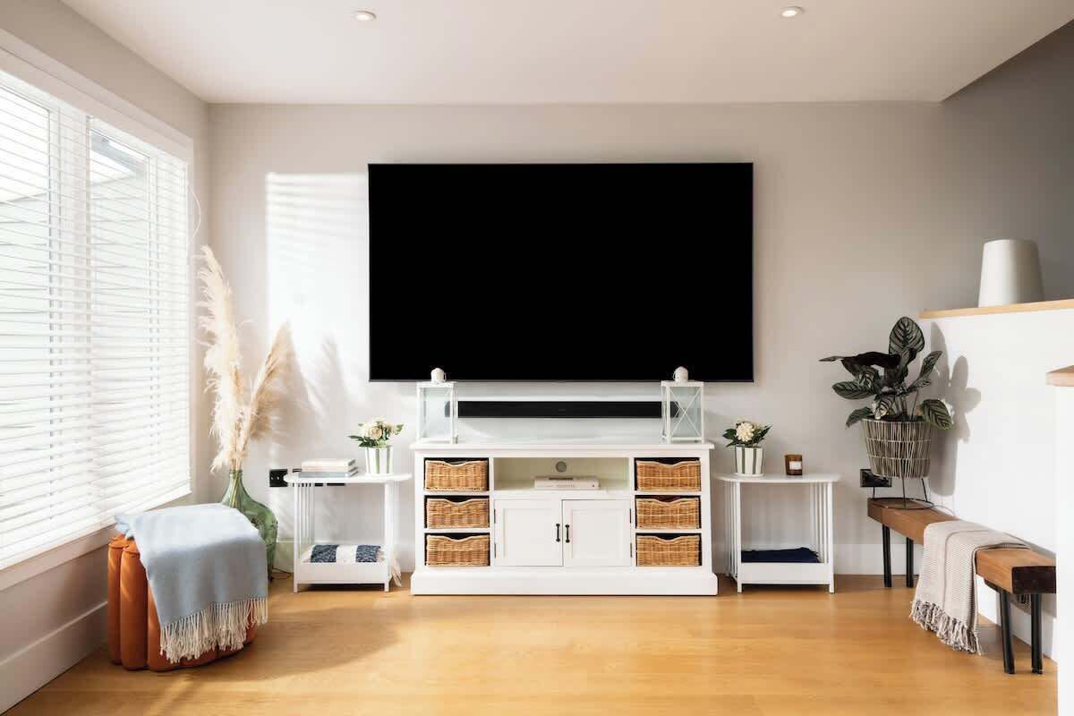 Un salon moderne avec un téléviseur à écran plat fixé au mur, un meuble de rangement blanc avec des paniers en osier, un banc en bois et une plante en pot.