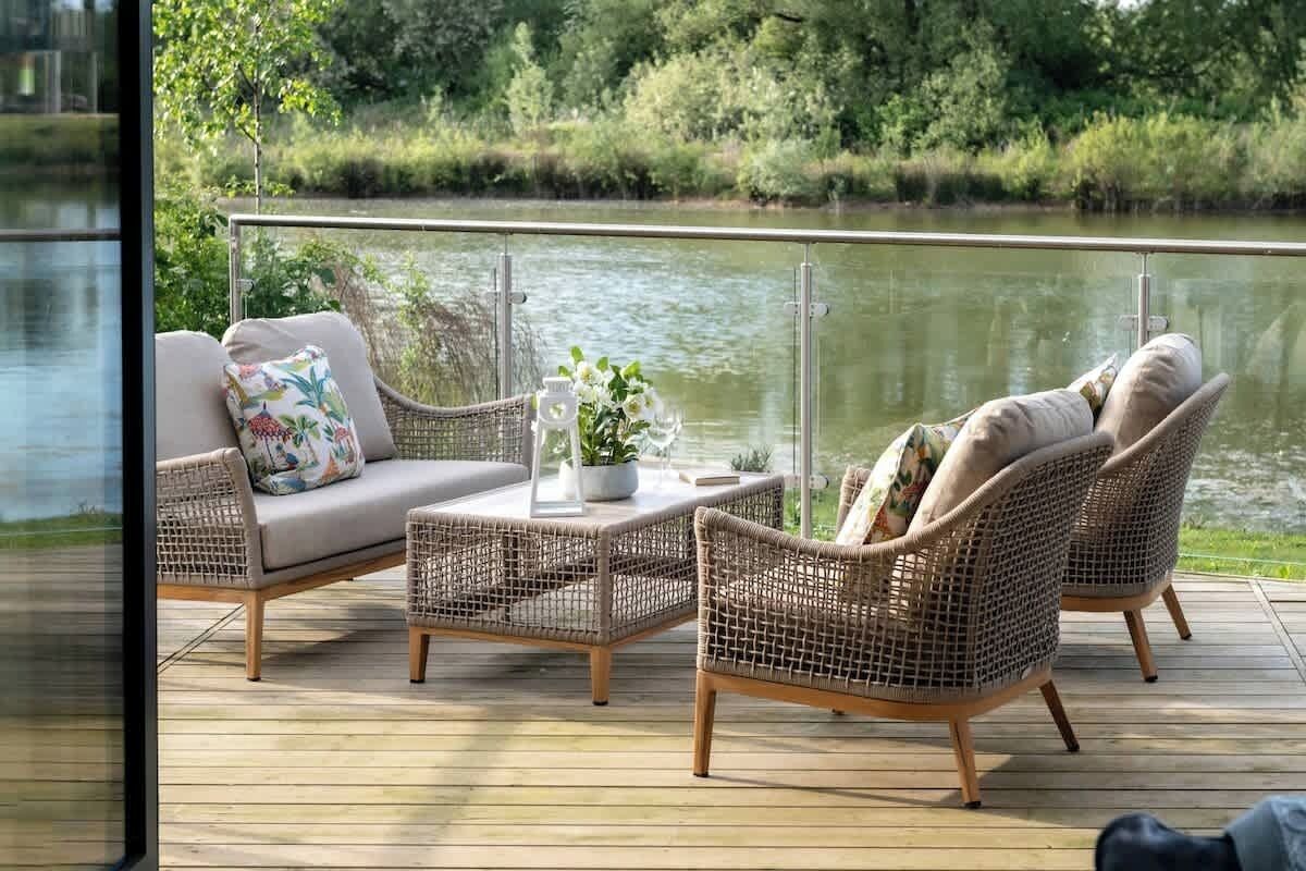 A deck with wicker furniture, a small table with a vase, and a view of a river.