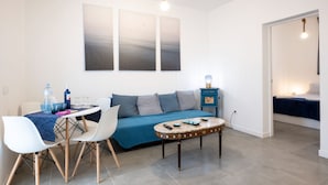 A modern living room with a sofa, coffee table, and dining area. There are three wall-mounted artworks above the sofa. - Océano: Acogedor y Luminoso Apartamento (Santa Cruz de Tenerife)