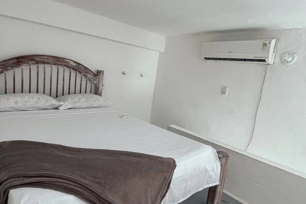 A single bed with a wooden headboard, white bedding, and a brown blanket. An air conditioning unit is mounted on the wall above the bed.