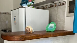 A kitchen counter with a white refrigerator, a decorative shell, and a green sign with text. - Casas Astro Rei (Cairu)